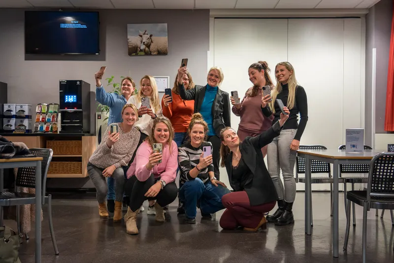 Een groep deelnemers poseert lachend met de telefoons in de lucht