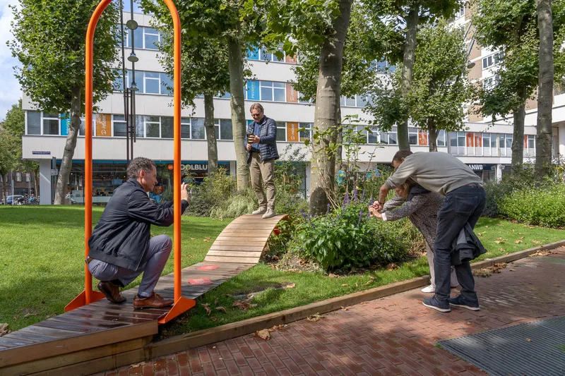 Deelnemers fotograferen laag bij de grond in een park, naast een oranje boog