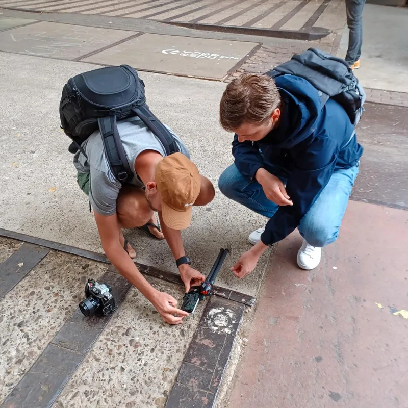 Twee deelnemers zitten op hun hurken op straat en fotograferen een spoorrail van dichtbij