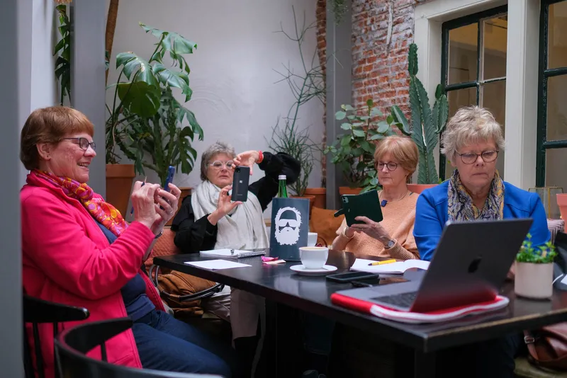Deelnemers aan tafel bekijken hun foto's op telefoon en laptop