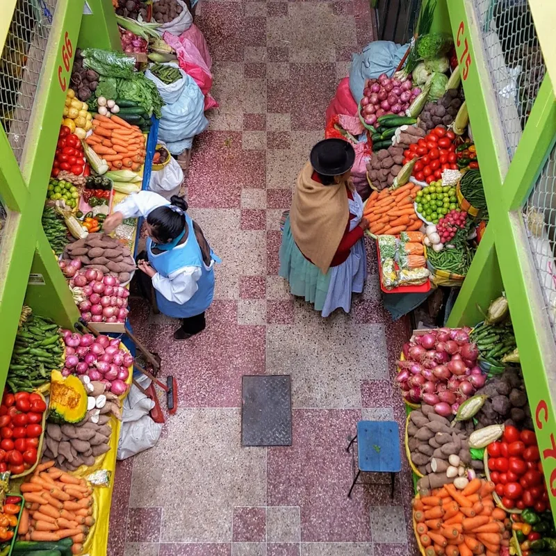 Een groentemarkt recht van boven gefotografeerd, met kleurrijke kramen en twee vrouwen