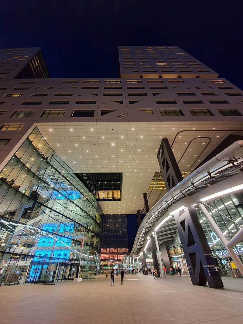 Modern gebouw met verlichte glazen gevels, van onderaf gefotografeerd bij avond