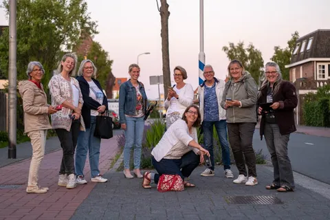Een groep collega's op straat bij schemering, een van hen fotografeert laag bij de grond