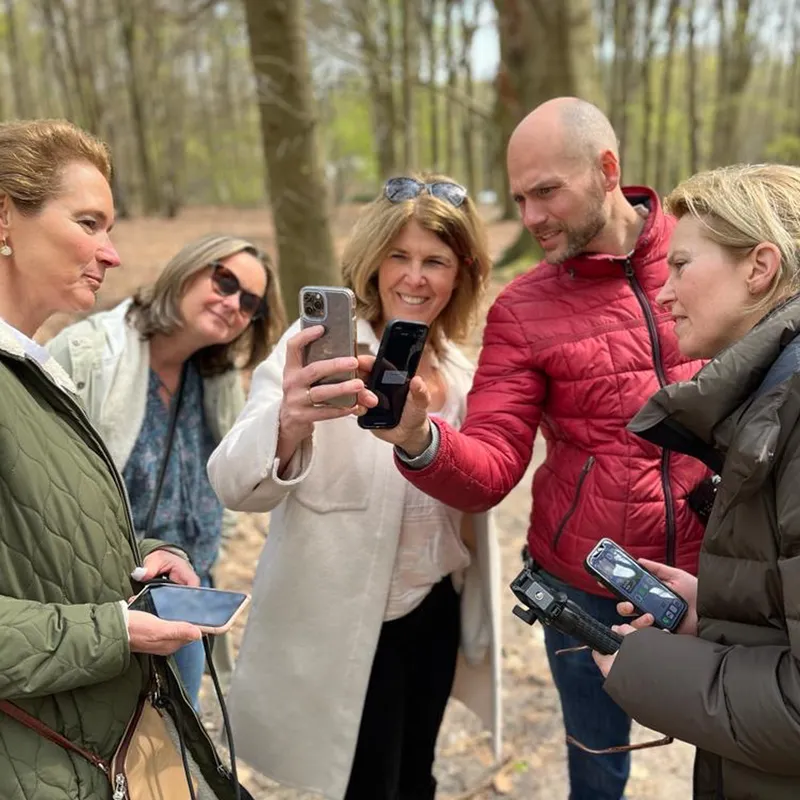 Deelnemers van een groepsworkshop in het bos kijken samen met Maarten naar hun telefoons