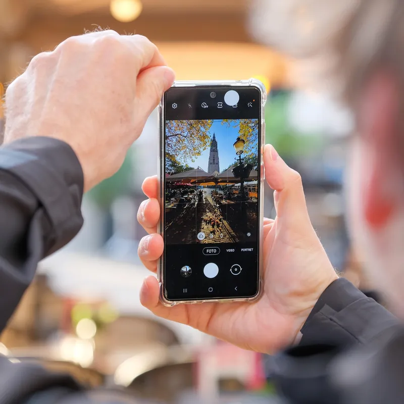Een hand houdt een telefoon omhoog met een kerktoren in beeld op het scherm
