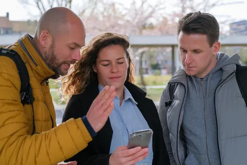 Maarten legt een deelnemer iets uit op haar telefoon, een derde kijkt mee