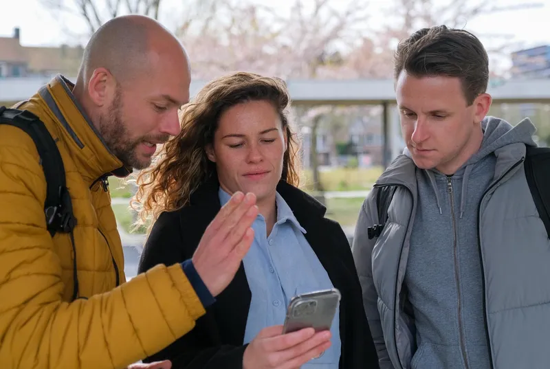 Maarten legt een deelnemer iets uit op haar telefoon, een derde kijkt mee